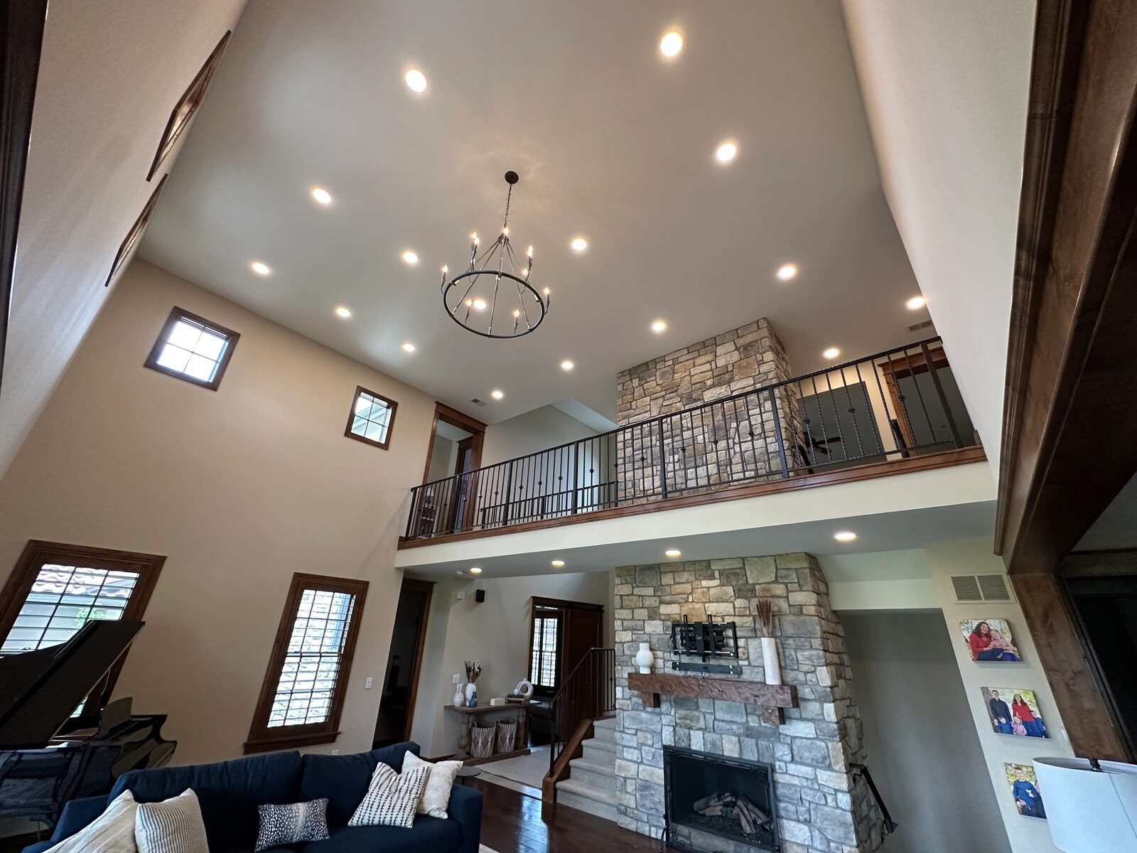 Vaulted great room with a ring chandelier and recessed ceiling lights above a stone fireplace.